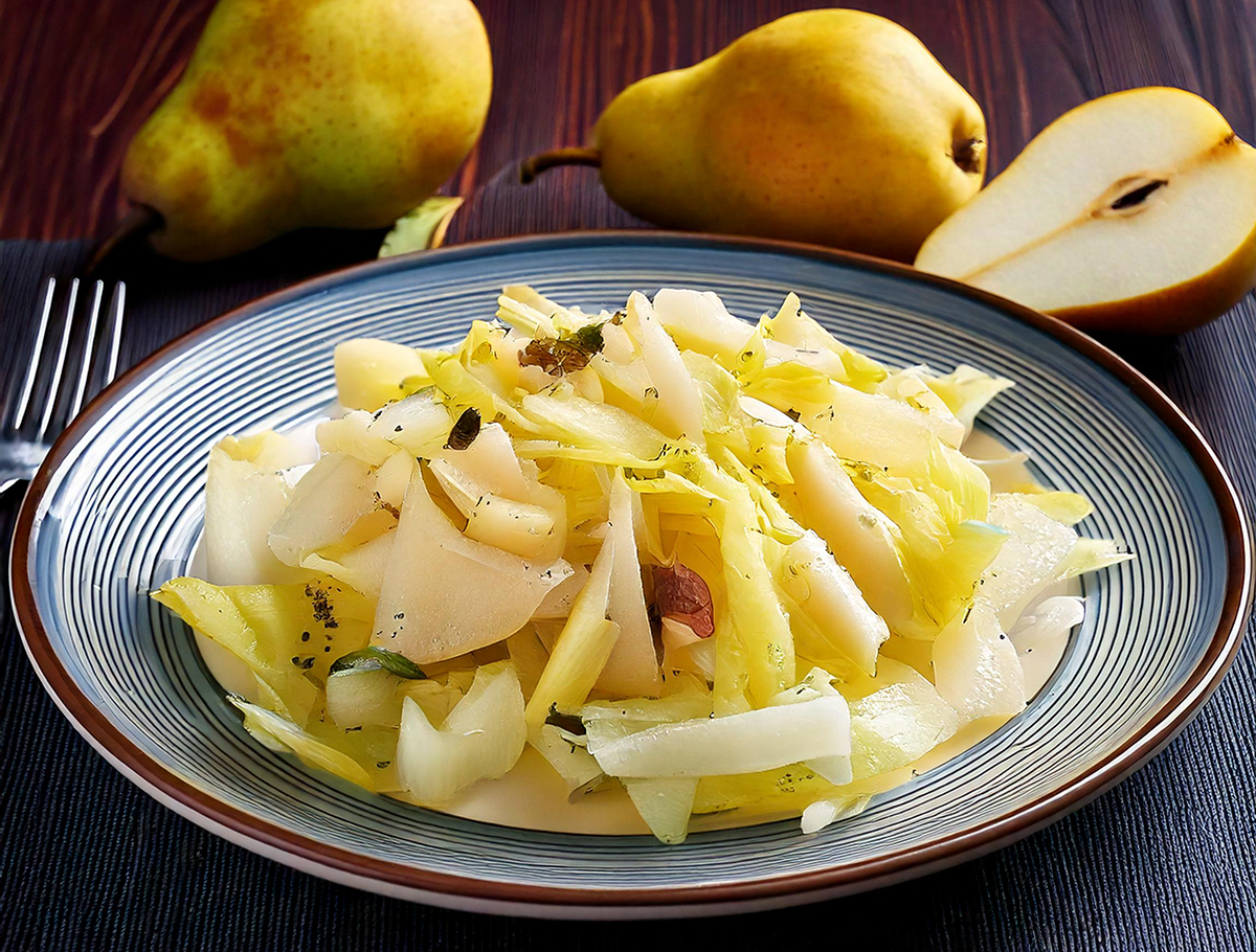 Teller mit Chicoreesalat, Birnenscheiben und Käse, im Hintergrund zwei ganze und eine halbierte Birne auf dunklem Untergrund.