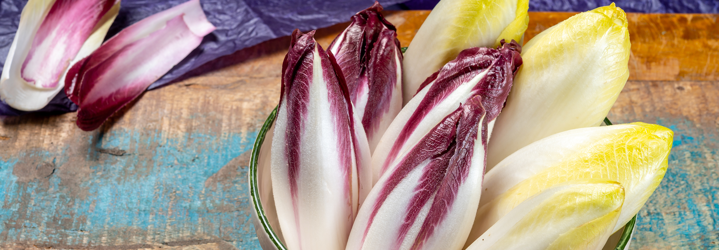 Schüssel mit mehreren Chicorée-Köpfen, einige rot-weiß, andere gelb-weiß, auf blau-braunem Untergrund.