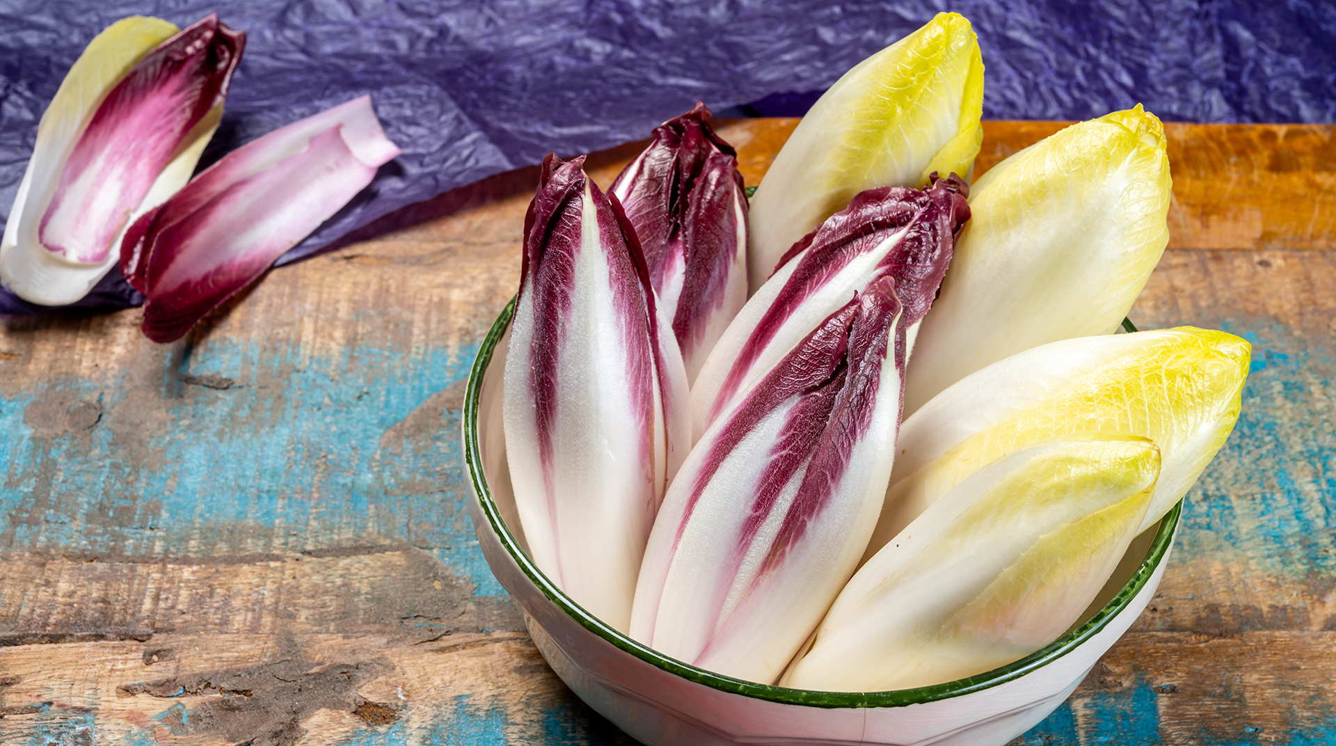 Schüssel mit mehreren Chicorée-Köpfen, einige rot-weiß, andere gelb-weiß, auf blau-braunem Untergrund.