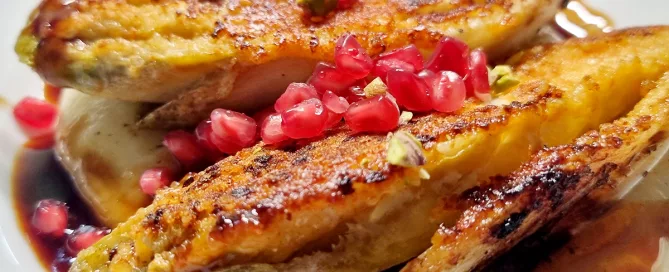 Knusprig gebratene Chicoréehälften auf einem Teller, garniert mit Granatapfelkernen und Pistazienstücken.