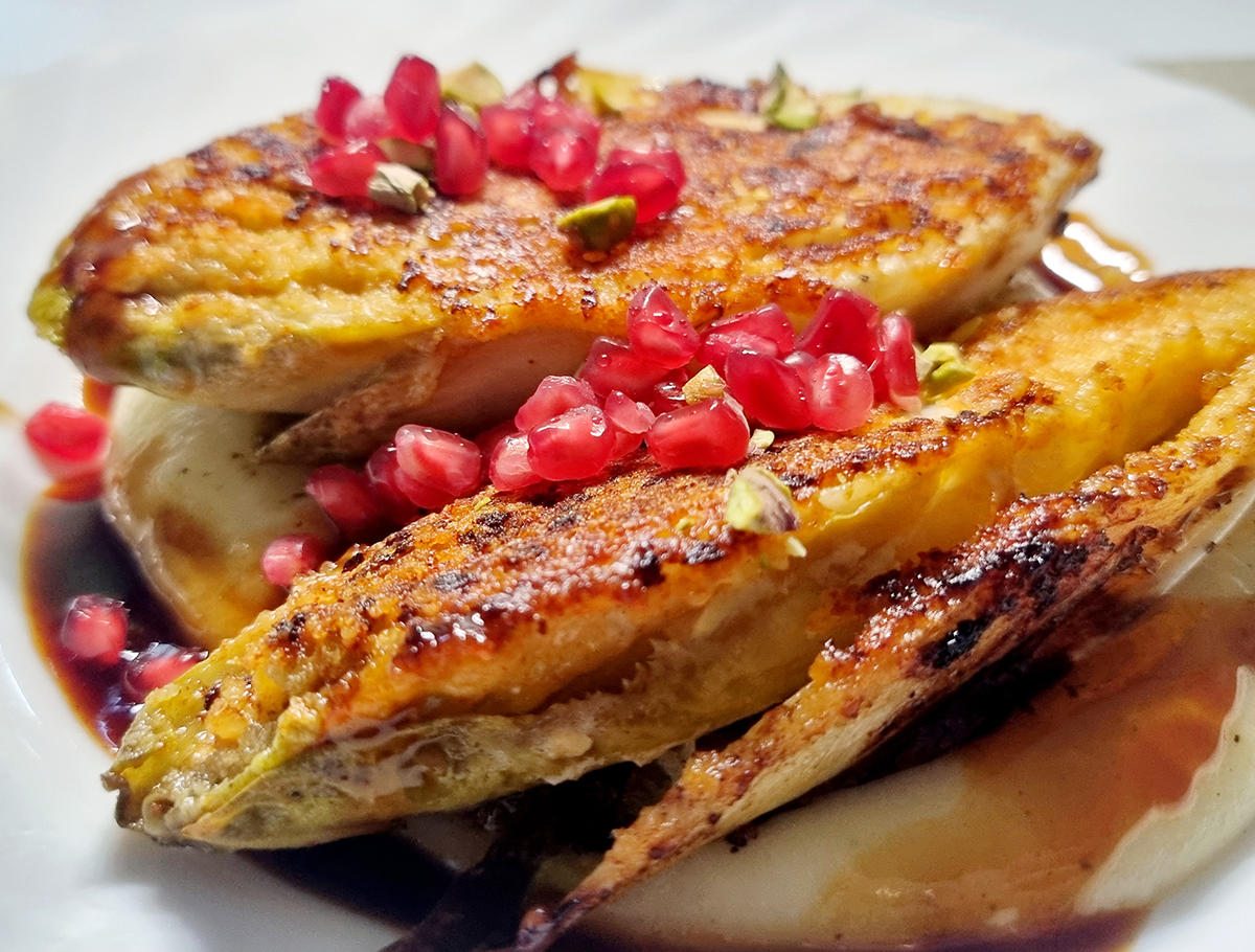 Knusprig gebratene Chicoréehälften auf einem Teller, garniert mit Granatapfelkernen und Pistazienstücken.