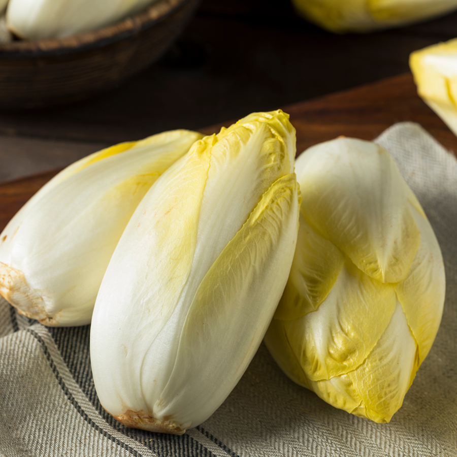 Drei frische, gelb-weiße Chicorée liegen auf einem Leinentuch auf einem Holztisch.